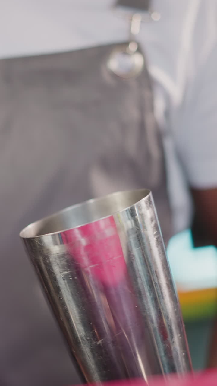 Barman puts ice cubes into shaker with scoop closeup. Black barkeeper prepares ingredients for cocktail. African American bartender works in nightclub