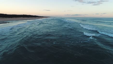 Luftaufnahme,-Die-Einen-Surfer-Verfolgt,-Der-Herauspaddelt,-Um-Bei-Sonnenaufgang-Einige-Wellen-Zu-Fangen,-Mit-Der-Nehrung-Im-Hintergrund-In-Southport-Gold-Coast,-Qld,-Australien