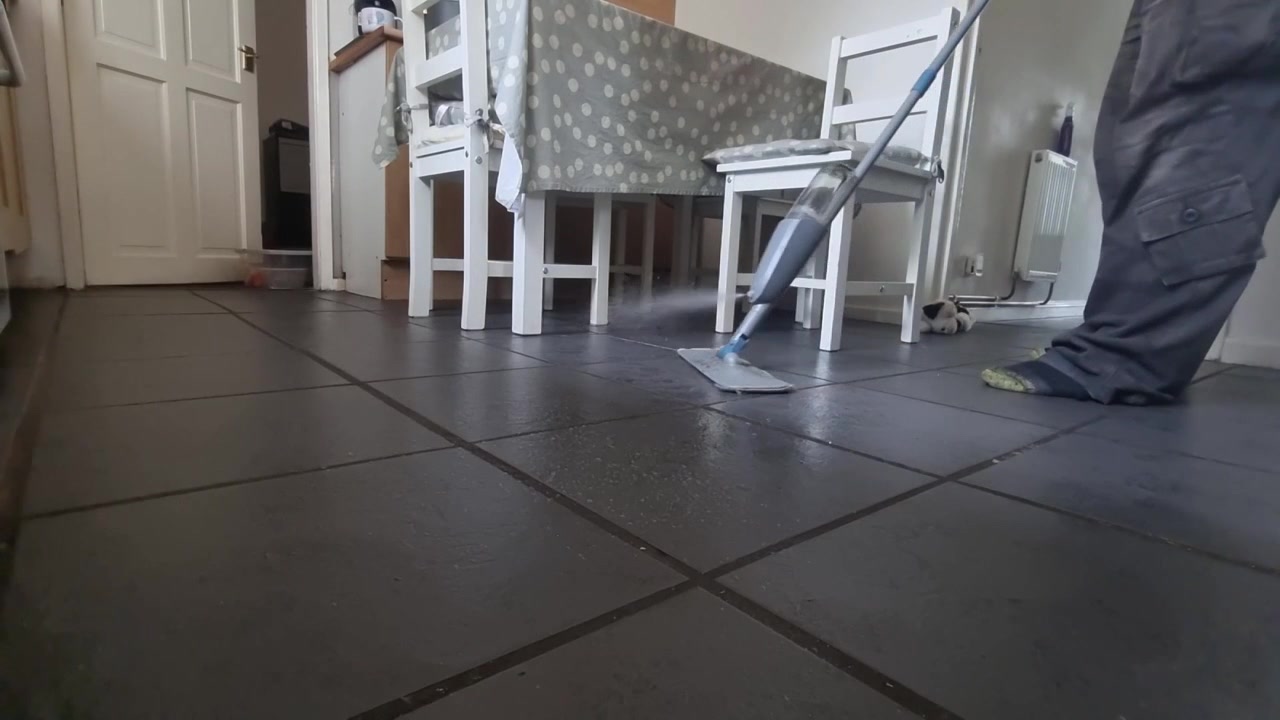 Low angle male wearing socks cleaning tiled kitchen flooring with antibacterial spray mop