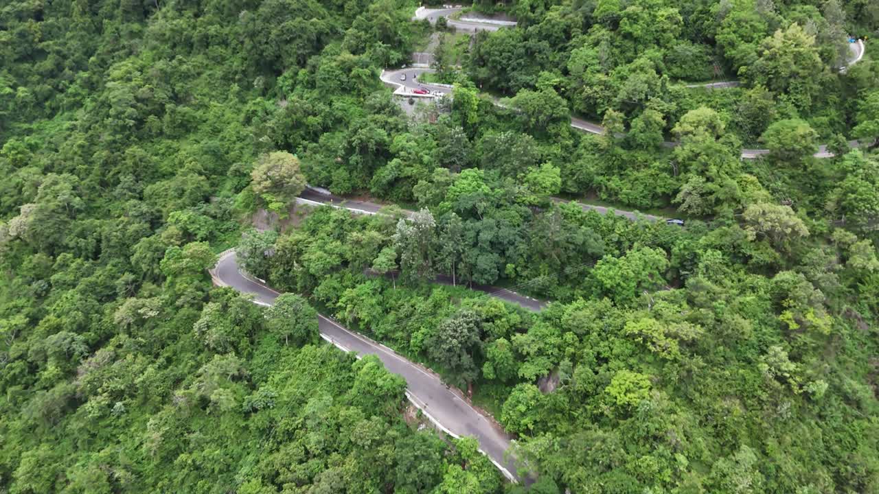 Mesmerizing view of a travel route designed with many sharp curves, suggesting an adventurous climb. The winding road is entirely surrounded by vibrant tropical forests. HIlls