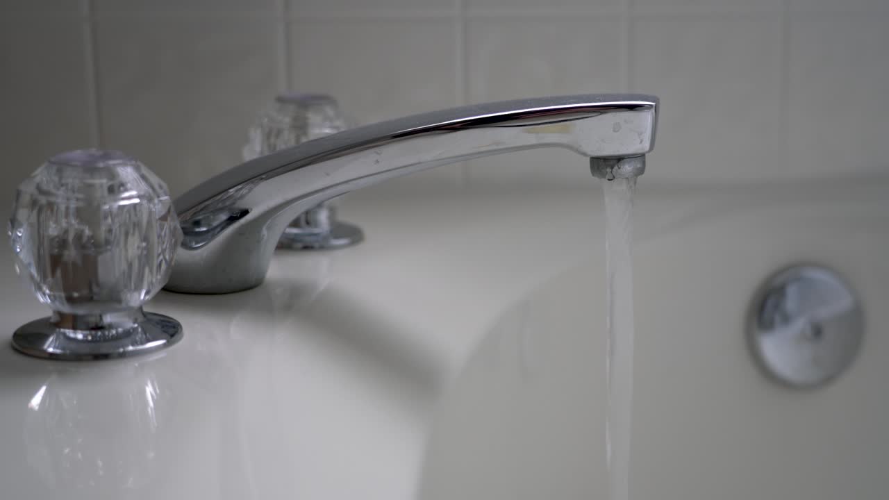 Water runs from a bathtub faucet into a bathtub.