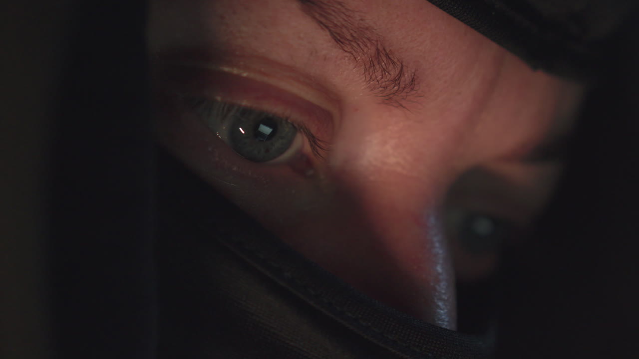 어두운 방에서 컴퓨터 화면을 보고 있는 마스크를 쓴 해커의 눈