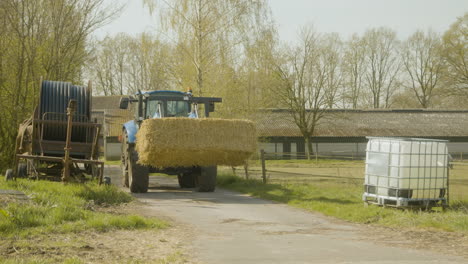 a tractor driving across a farm with a massive block of hay