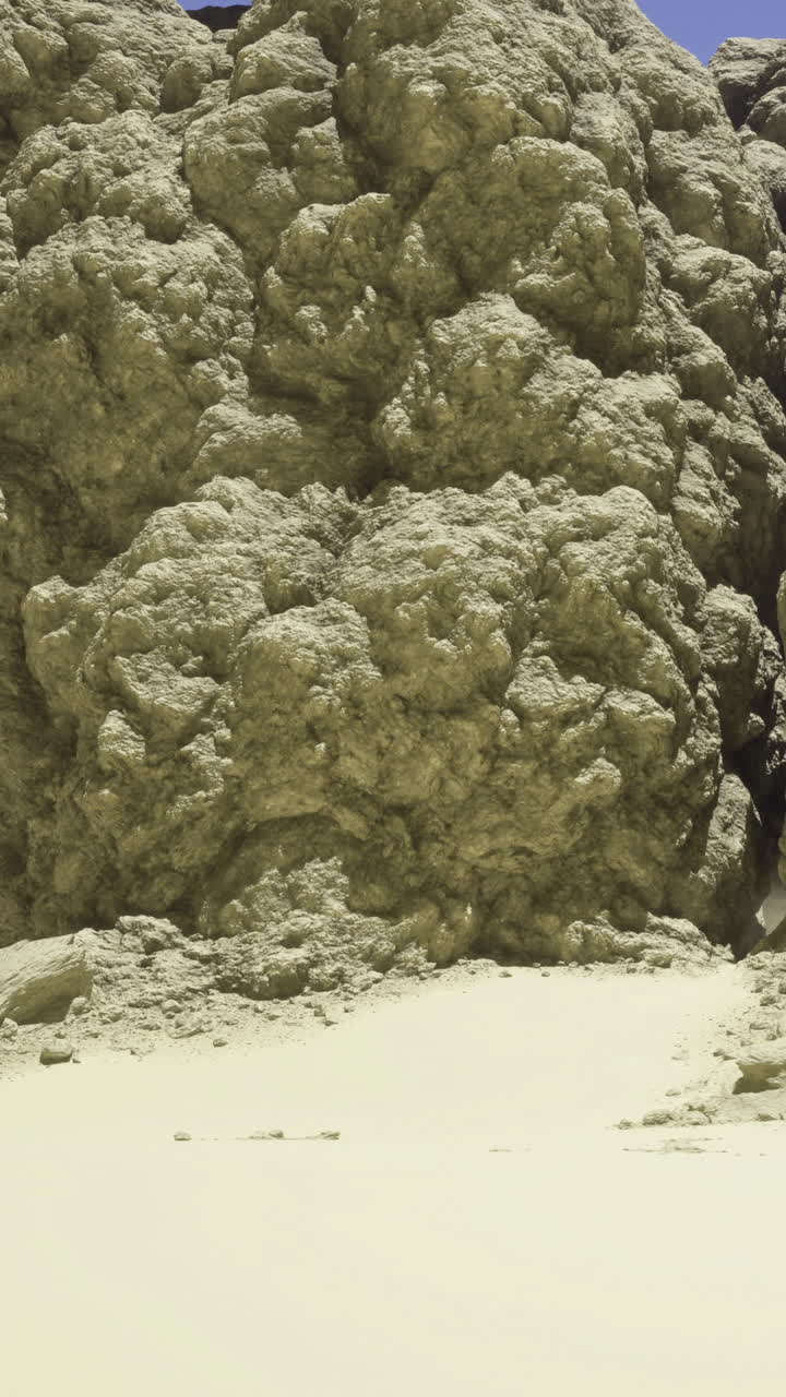 Una grande formazione rocciosa marrone si trova in una zona desertica arida sotto un cielo blu.