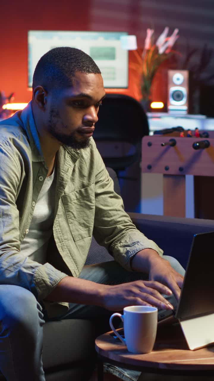 Vertical Video African American young adult working remotely on laptop under loft neon lights
