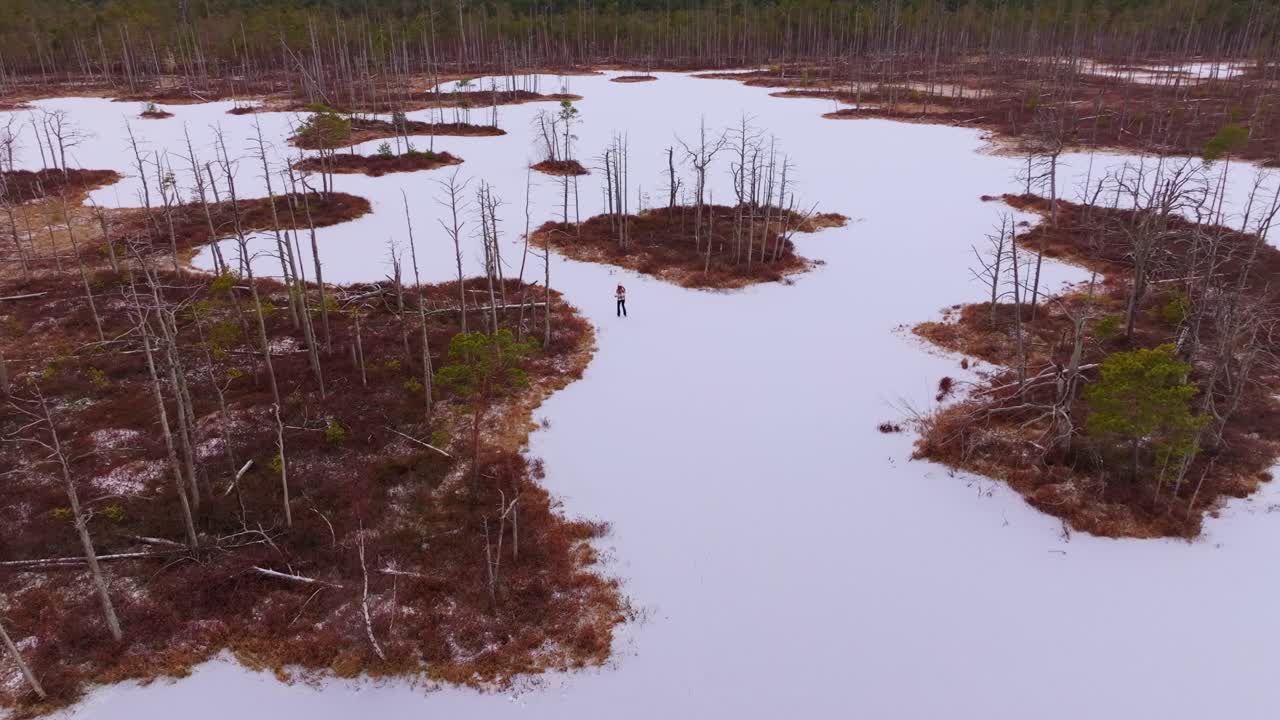 Aerial view of woman skating alone on frozen Cena Marsh Latvia lake in winter
