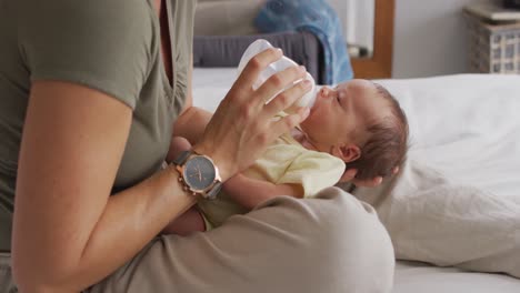 Video-Des-Mittelteils-Einer-Kaukasischen-Mutter,-Die-Ihr-Neugeborenes-Baby-Mit-Der-Flasche-Auf-Dem-Bett-Füttert