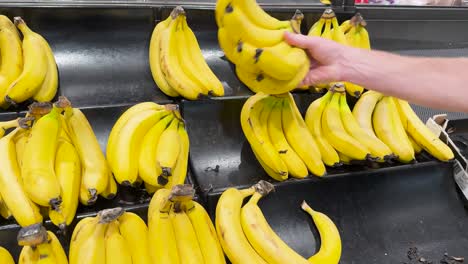 a hand picks bananas from a display