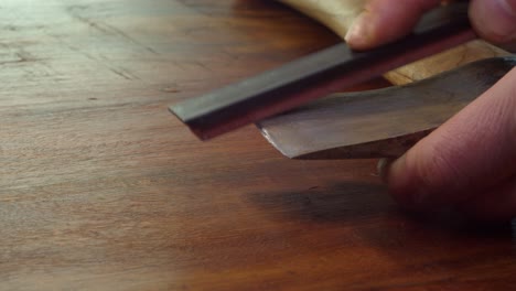 closeup view: man with whetstone sharpens old axe head on countertop