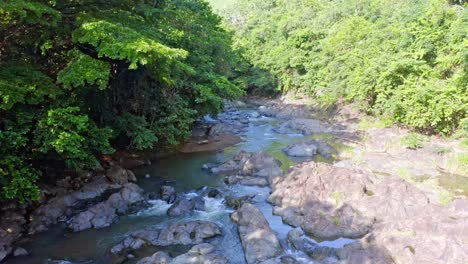 Aerial-flight-over-rocky-river-in-green-scenery-during-summer-day---Rio-Higuero-River,Dominican-Republic