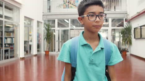 plano medio de un niño sonriente con anteojos caminando por el pasillo de la escuela, mirando a su alrededor y a la cámara