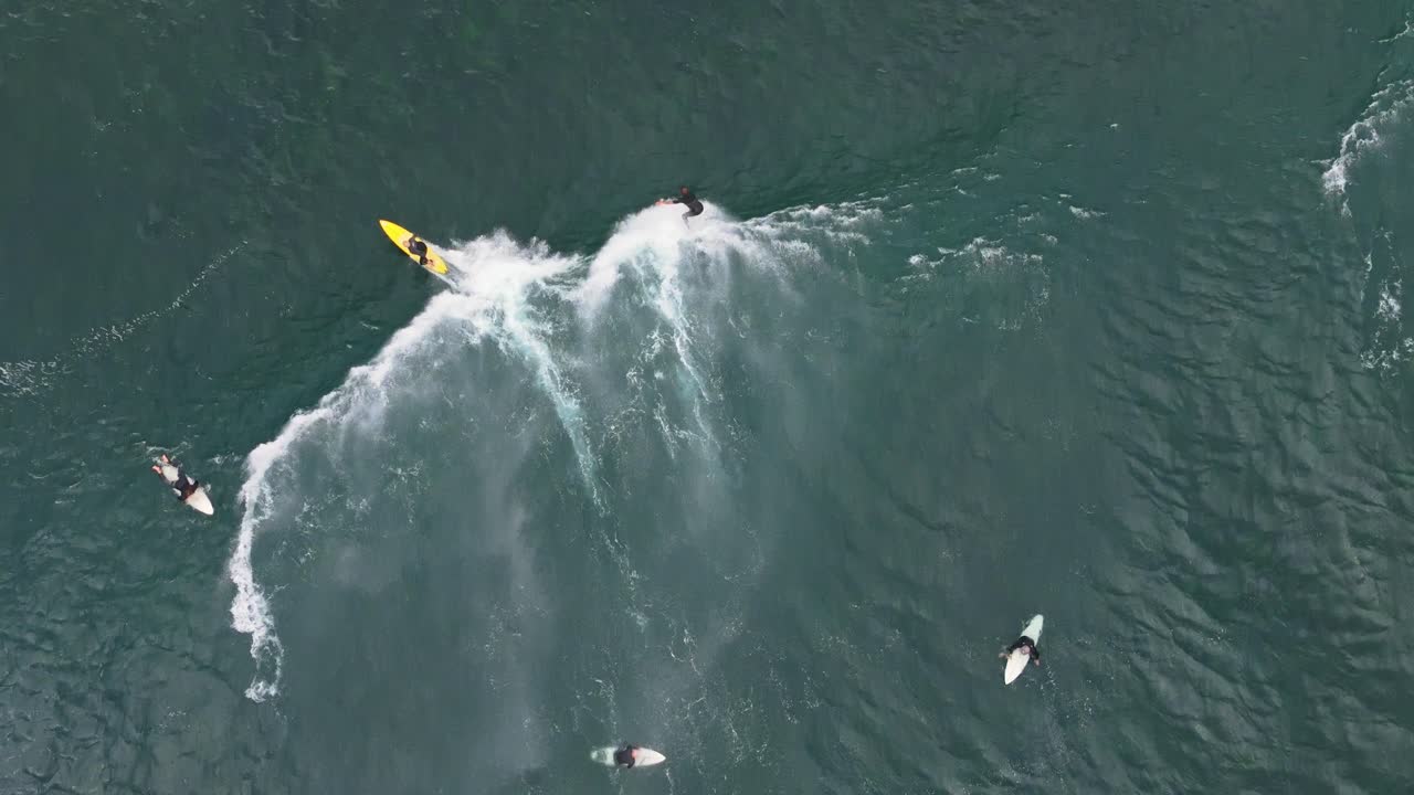 un video de un dron de arriba hacia abajo siguiendo a dos surfistas mientras atrapan una ola por encima de un arrecife poco profundo