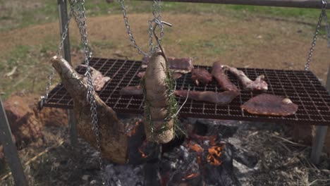 a handheld shot of grilling meat outdoors on a hook and a hanging grill