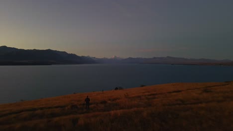 aerial dolly-out reveals man on top of ridge above lake pukaki