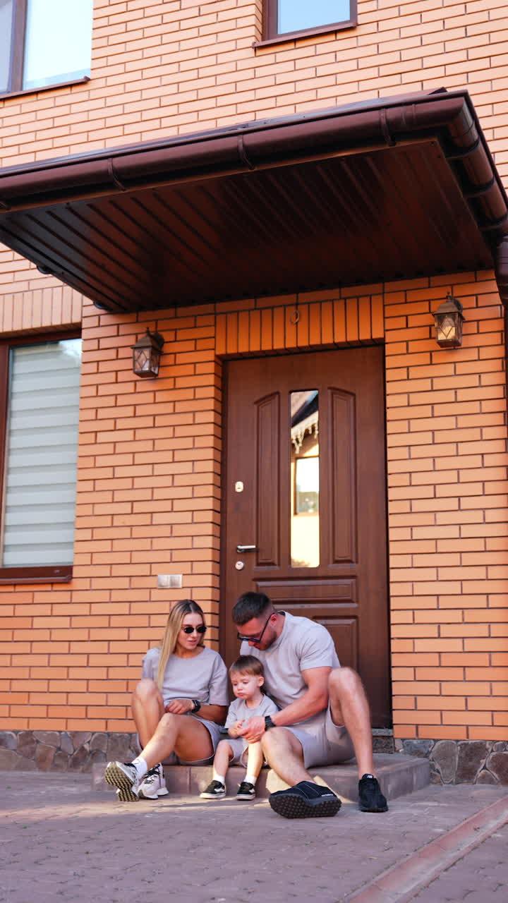 Man comes up to the doorstep to his wife and kid. Portrait of a lovely Caucasian family at the door to the house outdoors. Vertical video