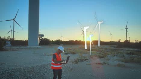 construction worker with smart laptop in front of wind turbines field install and plan digital new wind turbine in the light of sunset