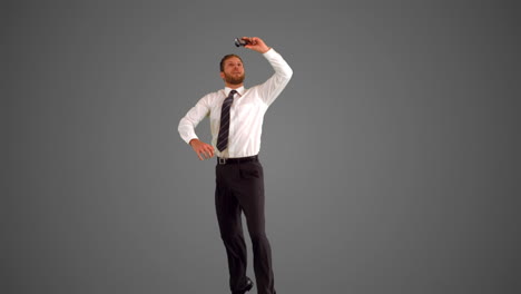 businessman leaping and taking self portrait on grey background