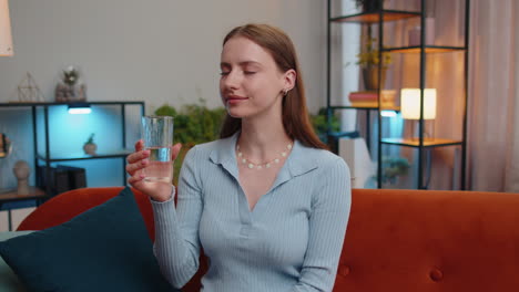 Una-Mujer-Joven-Sedienta-Sentada-En-Casa-Sosteniendo-Un-Vaso-De-Agua-Natural-Haciendo-Sorbos-Bebiendo-Agua-Sin-Gas