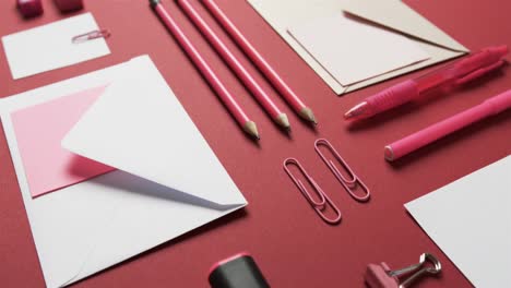 close up of pens, pencils and stationery arranged on red background, in slow motion