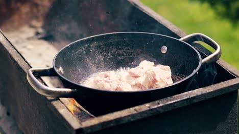 close-up slow motion pork meat is fried in saucepan on charcoal the person adds meat to the cauldron