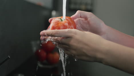 las manos de las mujeres lavan un tomate bajo el agua corriente del grifo. vídeo en 4k en cámara lenta