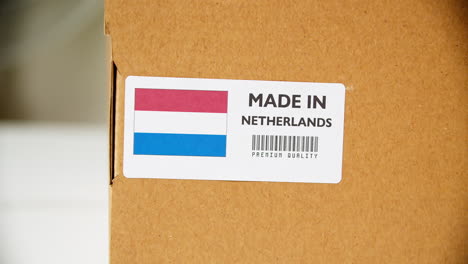 manos aplicando etiqueta de bandera hecha en holanda en una caja de cartón de envío con productos