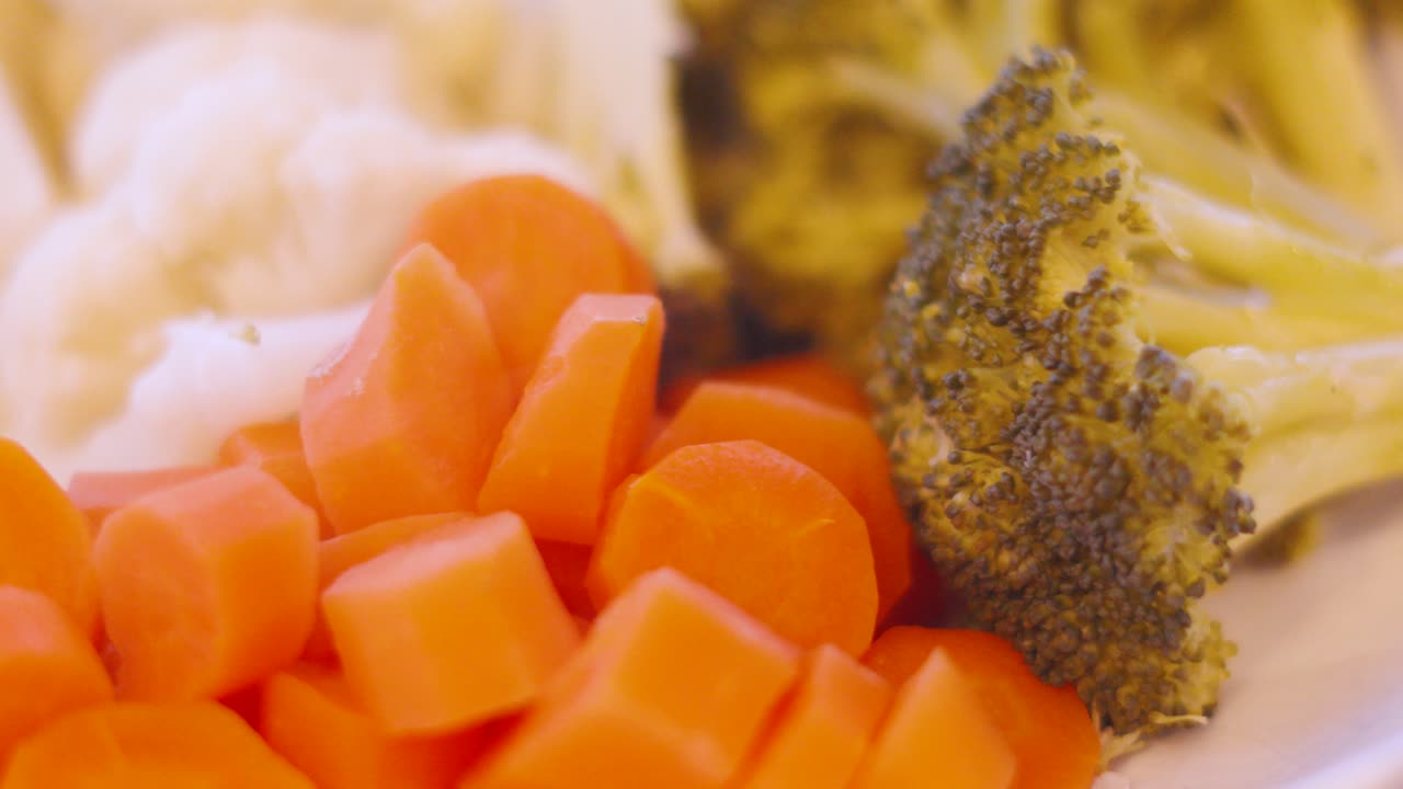 Cimette di broccoli, carote e cavolfiore appena cotti a vapore in una ciotola da portata sul tavolo da pranzo, pronti per essere serviti e mangiati. Verdure bollite per uno stile di vita alimentare sano 4K