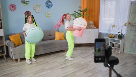 niños carismáticos filman historias en su teléfono móvil en casa, las amigas bailan con figuras de helado y macarrón frente a la cámara sobre un fondo de luces de colores