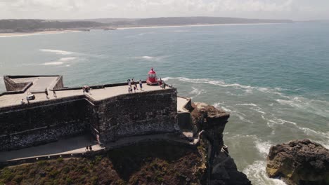 Vista-Aérea-Turistas-Explorando-El-Faro-De-Nazaré-Con-El-Paisaje-Marino-Como-Fondo