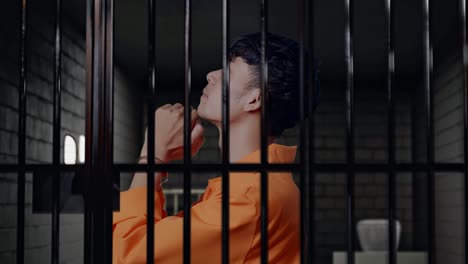 vista lateral de cerca de un prisionero masculino asiático con esposas reza por algo mientras está de pie en la prisión