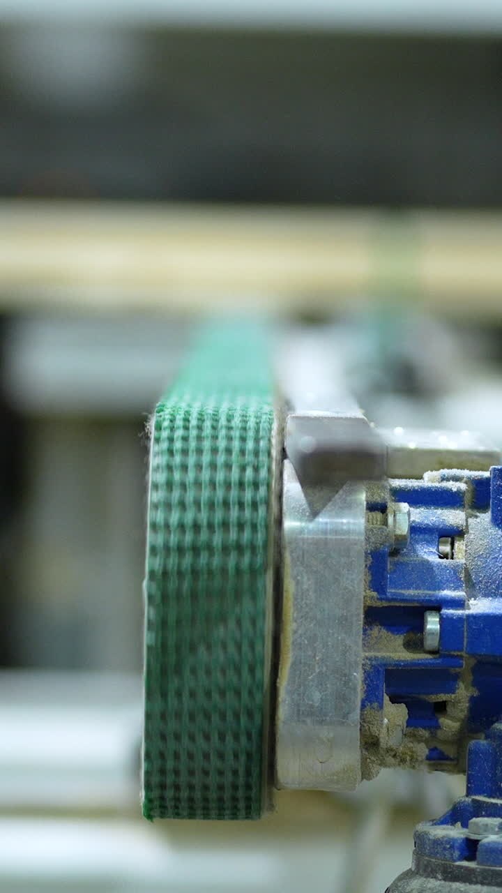Close up of a green textile conveyor belt moving on a blue industrial motor in a woodworking facility. Ideal for manufacturing and automation content