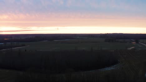 Aerial-ascend-over-dark-countryside-field-during-bright-sunset-sky-near-horizon