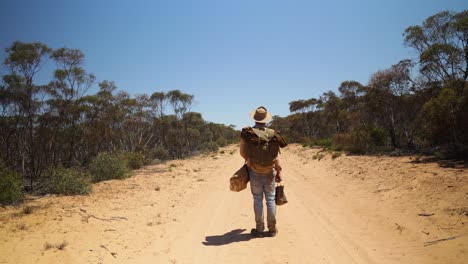 a historical looking swagman stand on a remote outback road in australia