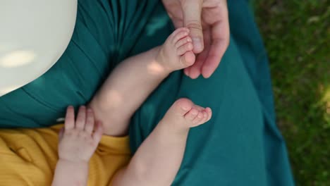 mano de la madre sosteniendo las piernas del bebé mientras está sentada en el parque