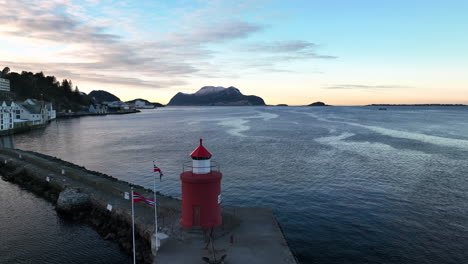 Norway-4K-Aerial-of-Ålesund-in-winter-slowly-pushing-on-over-and-past-Molja-Lighthouse-and-flaags-with-beatiful-sunset-in-the-background