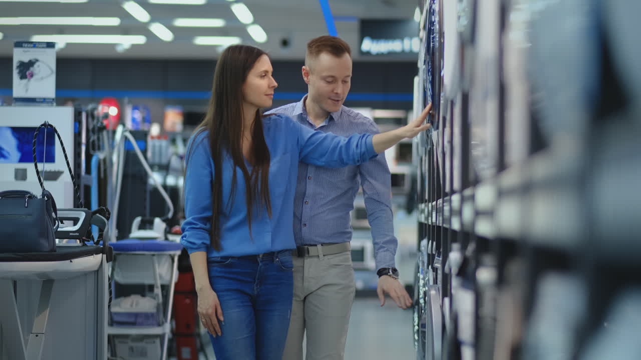A man and a woman open the door of the washing machine inspect the design and quality before buying in the store
