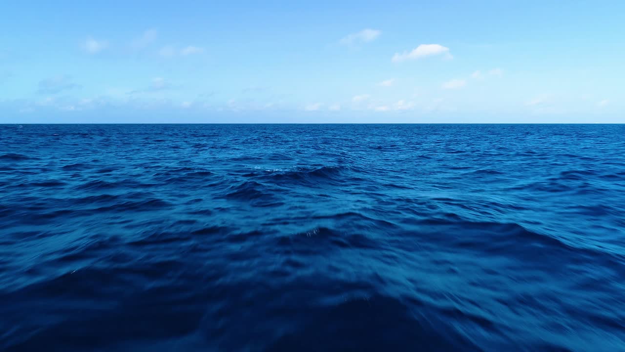 Texture dell'acqua di onde oceaniche blu profondo con nuvole nel cielo blu all'orizzonte, carrellata aerea con drone