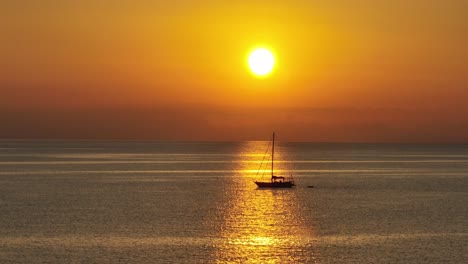 Vista-Lateral-De-La-Silueta-De-Un-Velero-Retroiluminado-Flotando-En-El-Océano-Abierto-En-Un-Rayo-De-Sol-Bajo-El-Cielo-Naranja-De-La-Hora-Dorada