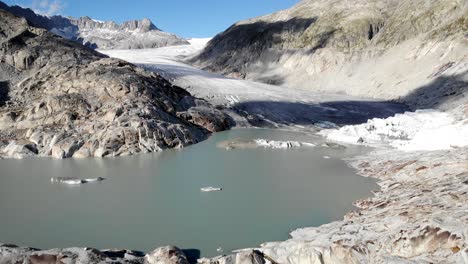 aerial flyover over the glacial lake and icebergs of rhone glacier near furka mountain pass at the border of valais and uri in switzerland towards the glacier's ice and crevasses