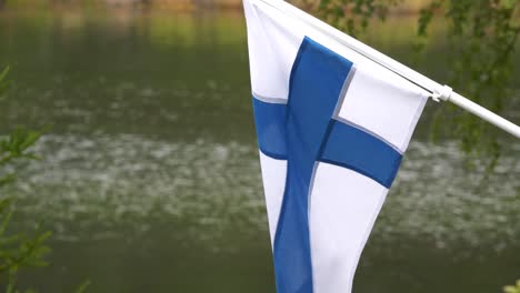 the flag of finland blowing in the wind at countryside cabin by the lake, slow motion tilting up