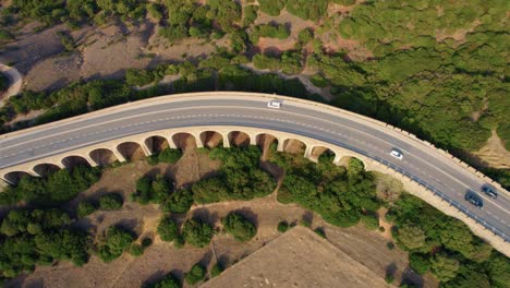 Top-down-aerial-drone-view-of-cars-passing-along-highway-through-the-European-countryside-at-sunset