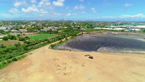 Excavator-loader-on-edge-of-sandy-dredged-deep-harbor-water-in-curacao-willemsted,-aerial-drone-dolly