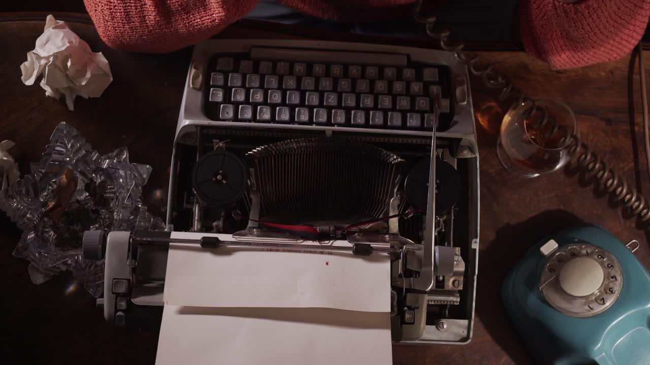 Author writes with typewriter at desk with rotary phone and cigar, overhead