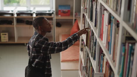 man browses for book on library shelf. dark-skinned student selecting literature for homework seen at university information center. guy perusing in bookstore