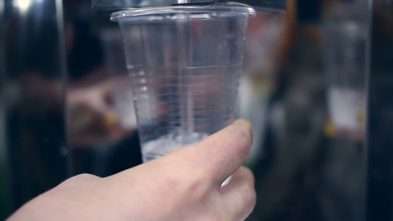 agua que fluye en una taza de plástico. primer plano de la mano sosteniendo la taza con agua