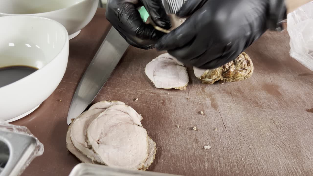 Detailed close-up of meat being cut on a wooden board by hand with black gloves, in a kitchen setting