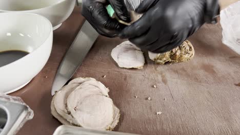 detailed close-up of meat being cut on a wooden board by hand with black gloves, in a kitchen setting