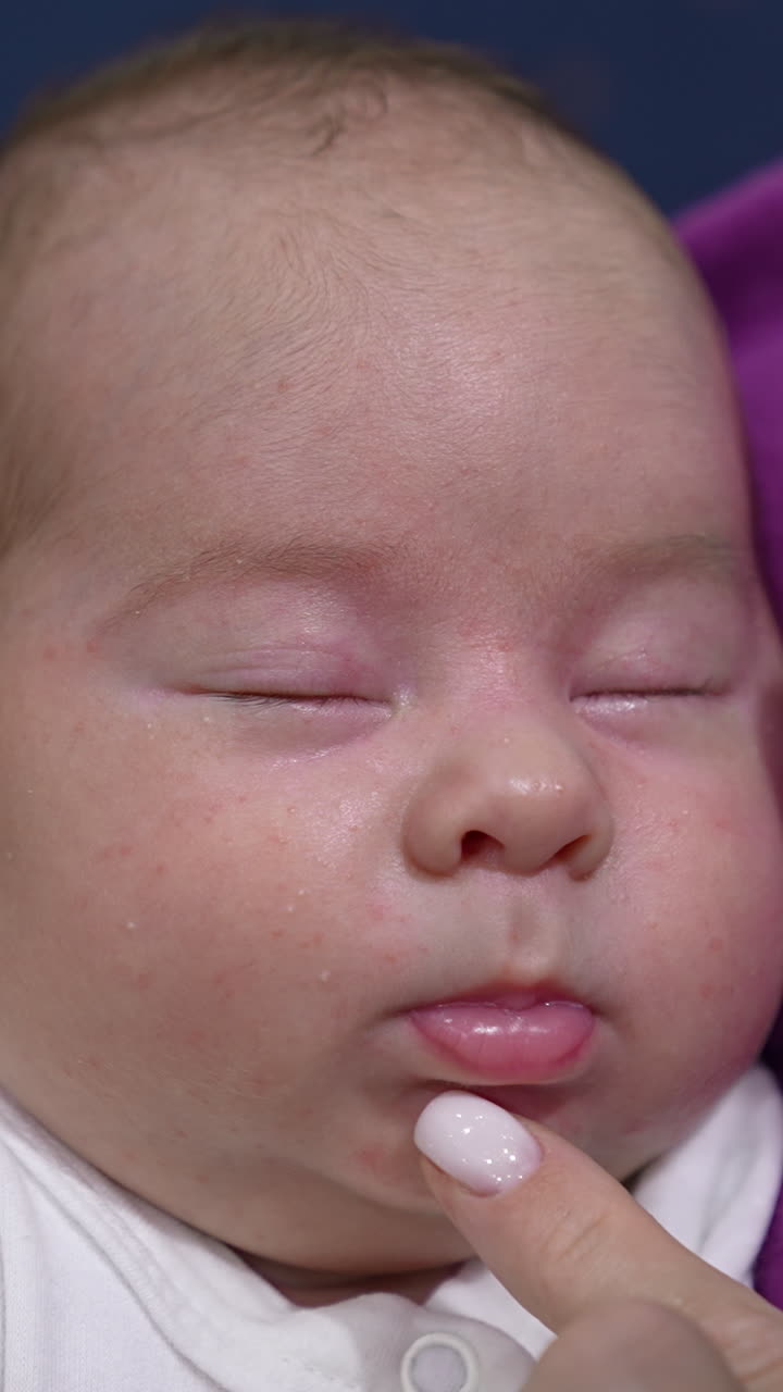 Sweet child sleeping tightly in his mom's hands. Caring momma trying to wake him up by touching little nose lovingly. Adorable sleeping newborn close up. Vertical video