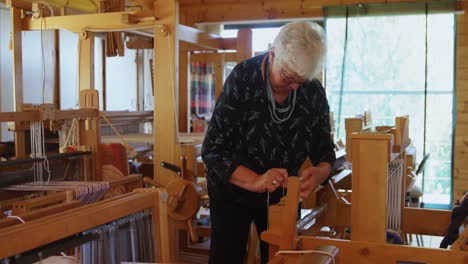 Front-view-of-old-caucasian-senior-woman-working-on-handloom-machine-in-a-workshop-4k