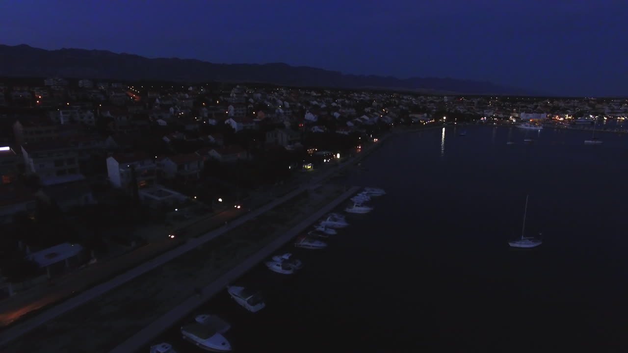 Aerial clip of the Croatia coast during the night, with boats berthed at the harbour.